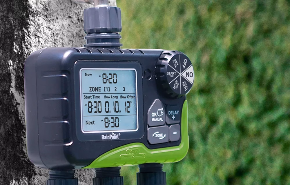 Lähivõte töötavast RainPoint niisutuskontrollerist, mis on kinnitatud puu külge, taustal roheline hekitaim