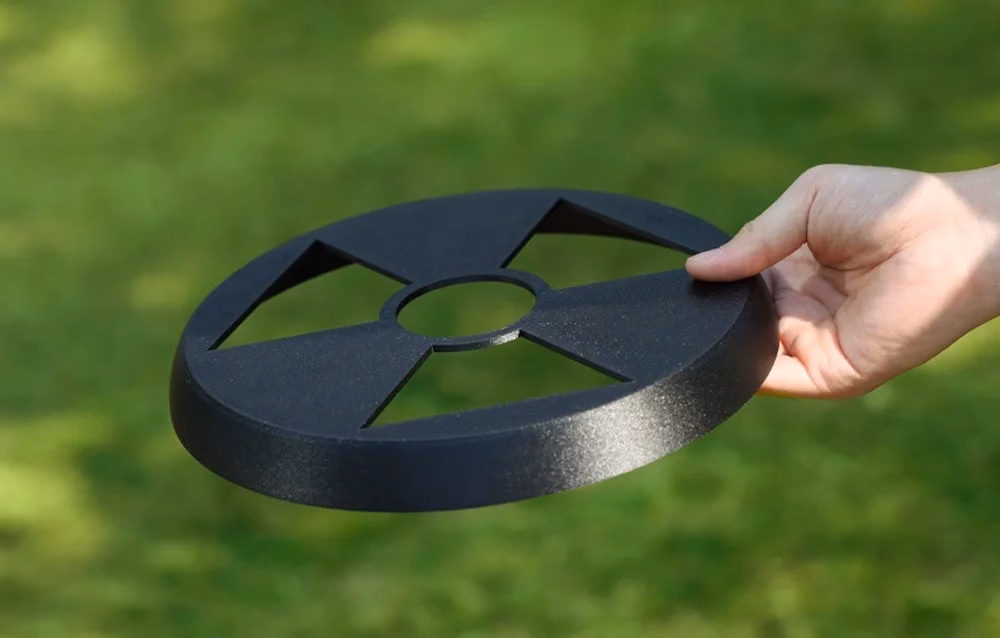 Käsi hoiab mustast Anycubic PETG-CF filamendist prinditud lendavat ketast