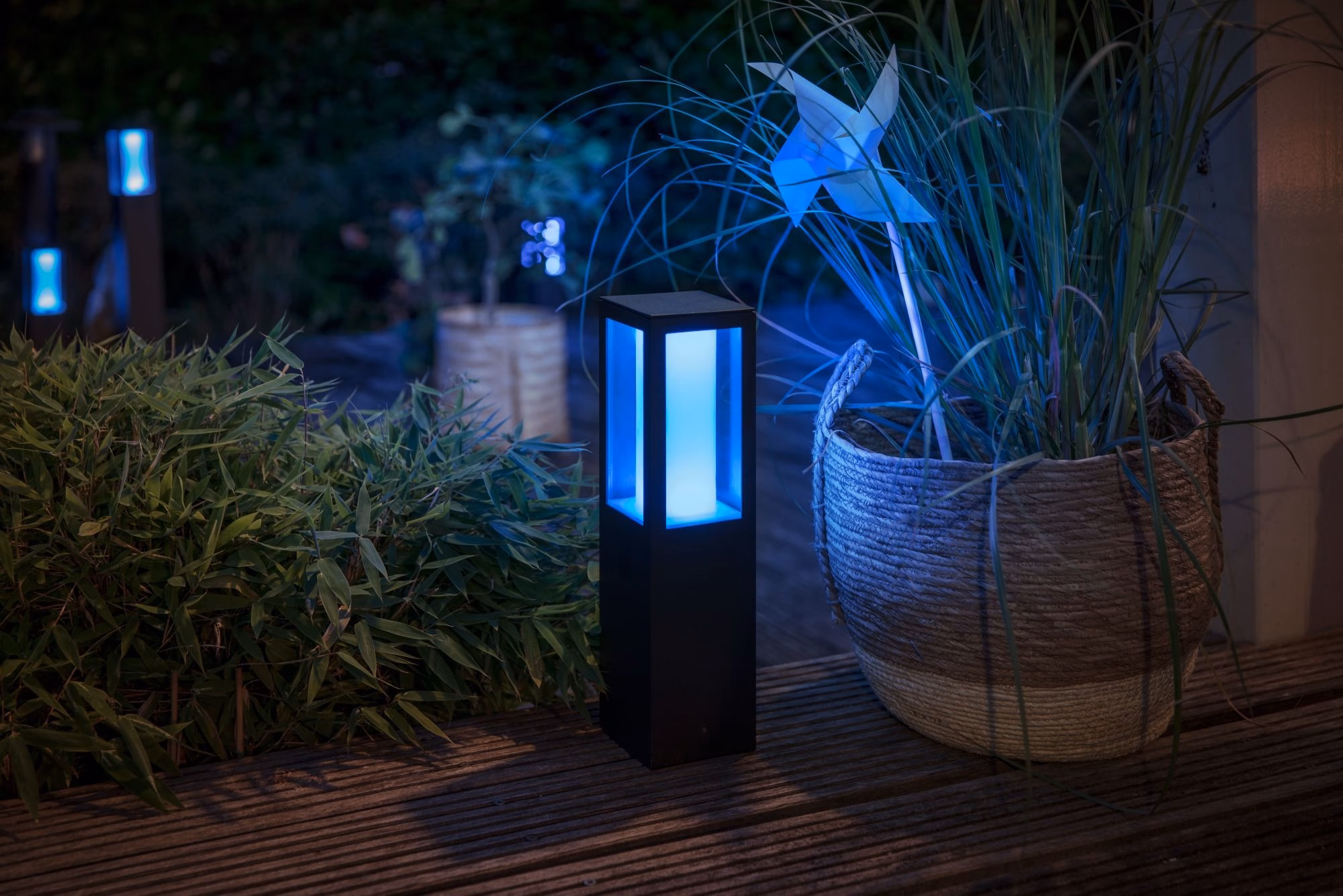 Philips Hue Impress Outdoor Pedestal sinise valgusega terrassil taimepoti kõrval