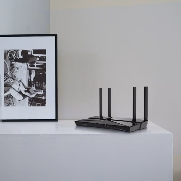 TP-Link Archer AX23 ruuter valgel kummutil raamitud pildi kõrval